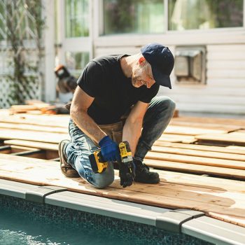 Handyman worker making patio outside close to a pool installing floor. A Handyman worker making patio outside close to a pool