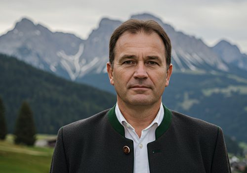 Portrait of a Man in Traditional Attire Against a Mountainous Landscape A portrait of a man wearing traditional attire, set against a breathtaking backdrop of majestic mountains. Calm atmosphere.