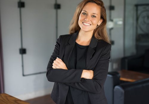 Smiling Beautiful Business Woman in Hotel Lounge Closeup portrait of smiling young beautiful brown-haired woman looking at camera and standing with her arms crossed in hotel lounge. Successful business woman concept. Front view.