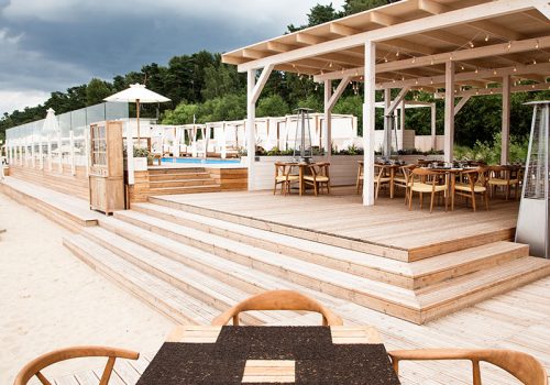 Terrace for relaxation on open air. Summer terrace for relaxation on open air in the summer beach with wooden chairs, tables, sofas and sun umbrellas.